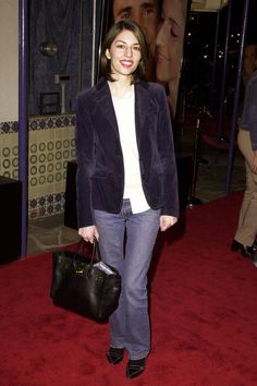 a woman holding a black purse and smiling at the camera while standing on a red carpet