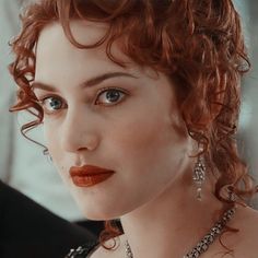 a close up of a woman with red hair and jewelry on her neck, looking at the camera