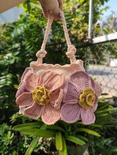 a hand holding a pink crocheted purse with flowers on the front and side