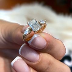 a woman's hand holding an engagement ring with two diamonds on it and the middle finger