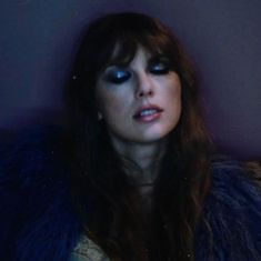 a woman with long hair and blue eyes wearing a fur coat in front of a wall