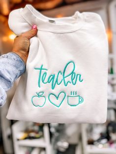 a person holding up a t - shirt with the word teacher on it in green ink