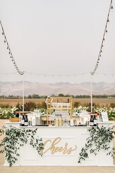 an outdoor bar is decorated with greenery and lights for a wedding reception in the desert