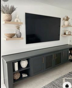 a flat screen tv mounted to the side of a wall in a living room with shelves