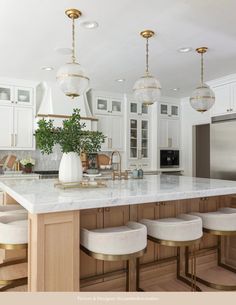 a large kitchen with white cabinets and marble counter tops, gold accents on the island