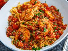 a white bowl filled with pasta and shrimp on top of a table next to utensils