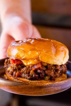 a close up of a person holding a plate with a sloppy joe sandwich on it