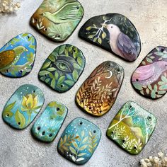 six painted rocks with birds and leaves on them sitting on a cement surface next to flowers