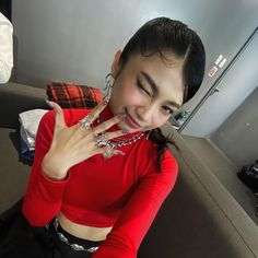 a woman in a red shirt is posing for the camera with her hand on her chest