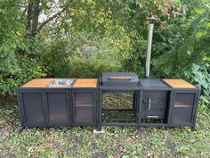 an outdoor bbq grill in the middle of some grass with trees and bushes behind it