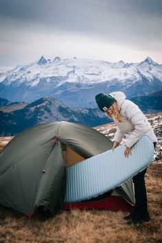 a man is setting up his tent on the top of a mountain with mountains in the background