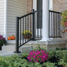 the front porch is decorated with flowers and pumpkins on the side walk, along with an iron railing