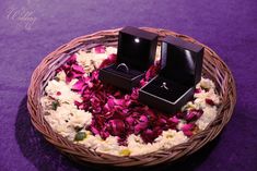 two wedding rings sitting on top of a basket filled with rose petals and petals in it