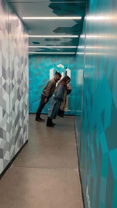 two people are standing in a blue and white hallway with geometric designs on the walls