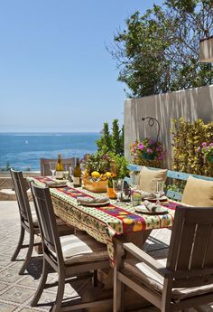 an outdoor dining table with flowers on it and the ocean in the backround