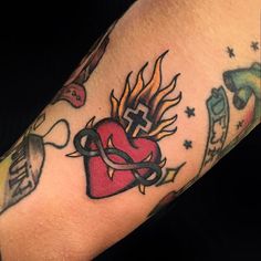 an arm with tattoos on it that has a red heart and cross in the middle