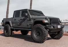 a black jeep parked on the side of a road near some water and palm trees