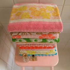 towels stacked on top of each other on a pink stool in front of a tiled wall