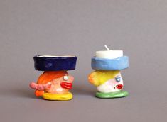 two small ceramic figurines sitting next to each other on a gray surface, one with a candle in it's mouth