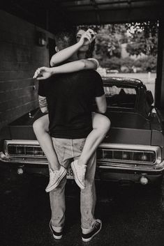 a man and woman sitting on the back of a car in front of a garage