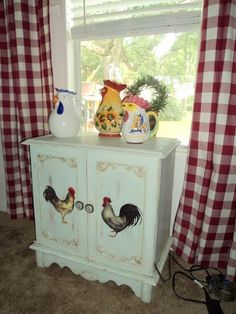 a white cabinet with roosters painted on it in front of a red and white checkered window