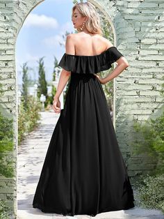 a woman standing in front of an archway wearing a black dress with off the shoulder sleeves