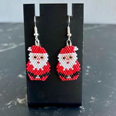 a pair of santa claus beaded earrings sitting on top of a black stand next to a white wall