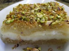 a white plate topped with a piece of cake covered in nuts and pistachio