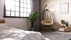 a bedroom with a hanging chair, bed and potted plant in the corner on the floor