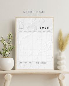 the modern estate calendar is displayed on a shelf next to a vase with flowers in it