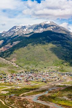 an aerial view of a small town in the middle of a mountain range with snow capped mountains behind it