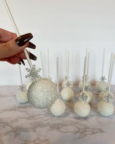 a hand is picking up some cake pops with snowflakes on them and candy canes in the foreground