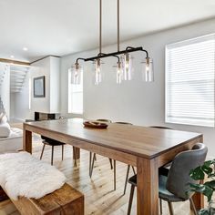 a dining room table with four lights hanging from it's center and two chairs at the end