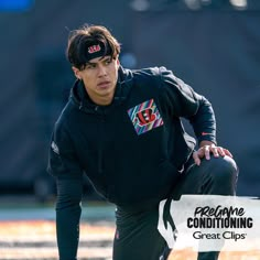 a young man kneeling down on top of a football field wearing a black hoodie