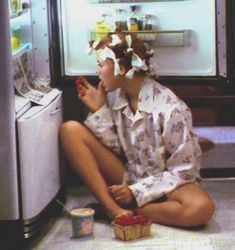 a woman sitting on the floor in front of an open refrigerator