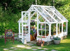 a small white greenhouse sitting in the middle of a yard with potted plants inside