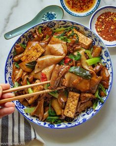 a person holding chopsticks over a bowl of food with meat and veggies