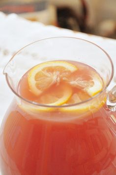 a pitcher filled with liquid sitting on top of a table next to a slice of lemon