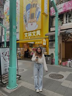 a woman is standing on the sidewalk in front of a building with an advertisement behind her