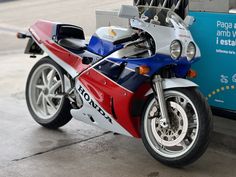 a red, white and blue motorcycle parked next to a gas pump