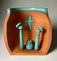 a small ceramic sculpture of a cross and two candlesticks in a bowl on a table