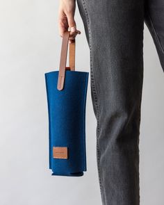 a person is holding a blue bag with leather handles and the bottom has a brown strap