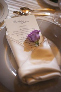 a purple flower is placed on top of a folded menu and place setting for an event