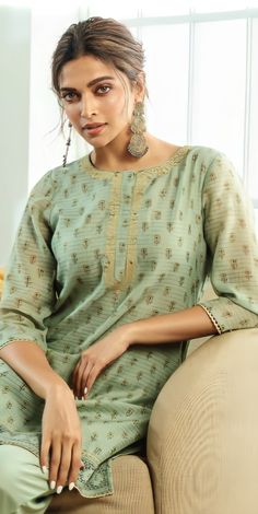 a woman sitting on top of a couch wearing a green shirt and pants with earrings