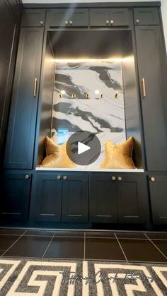 a room with black cabinets and gold pillows on the floor, in front of a marble wall