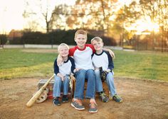 three young boys sitting on a bench with baseball equipment in front of them and the sun behind them