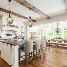 a large kitchen with white cabinets and wooden beams on the ceiling, along with gray bar stools