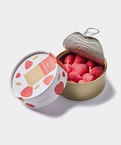 a tin filled with lots of pink balls next to a metal container full of strawberries