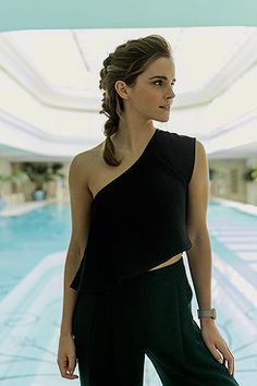 a woman standing in front of a pool wearing black pants and a one shoulder top