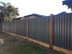 a fence that is next to a house and grass in the foreground with palm trees behind it